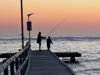 Fishing off the jetty at sunset .